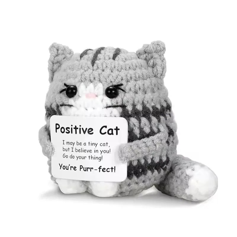 Crocheted cat plush toy with a sign reading 'Positive Cat' on a white background