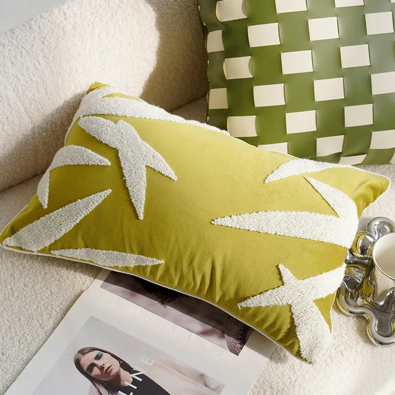 Green pillow with white leaf patterns on a couch next to a coffee cup and magazine.