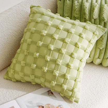 Green checkered pillow on a beige sofa with a green blanket.