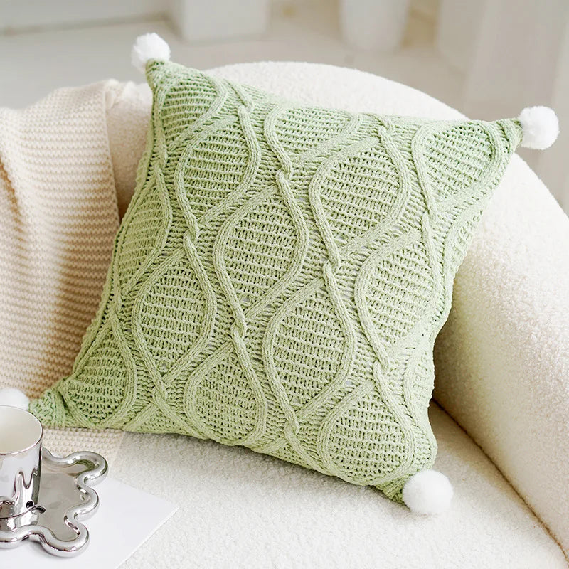 Green knitted pillow with pom-pom details on a beige sofa