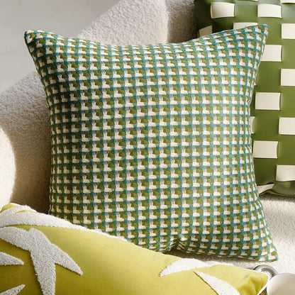 Green checkered pillow on a couch with a patterned wall in the background