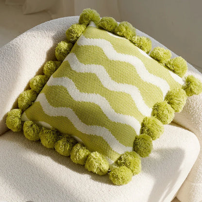 Green and white striped pillow with pom-pom trim on a white surface