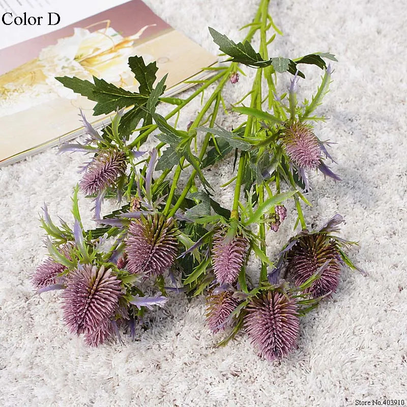 Purple thistle flowers with green leaves on a textured white surface
