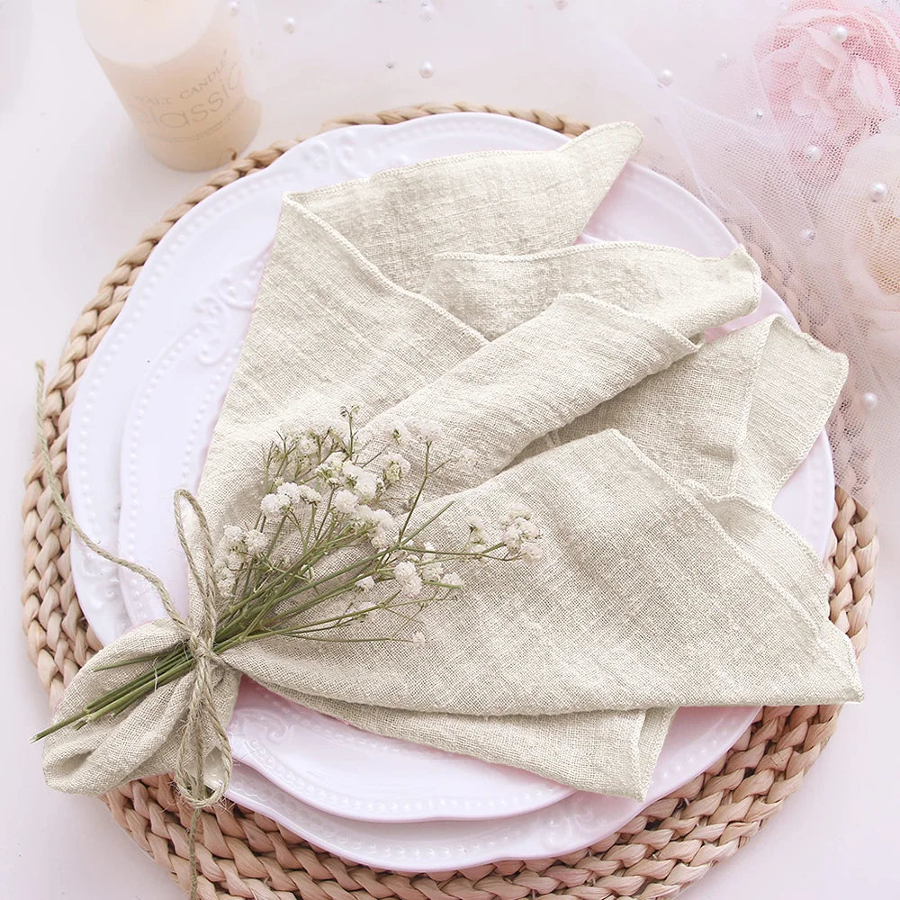 Folded light green napkin with a small bouquet of flowers on a white plate, placed on a woven mat.