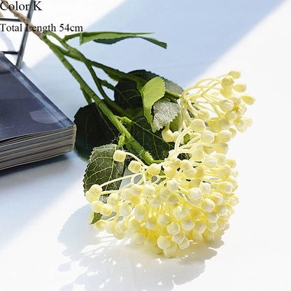 Artificial flower branch with green leaves and yellow flowers on a white surface.