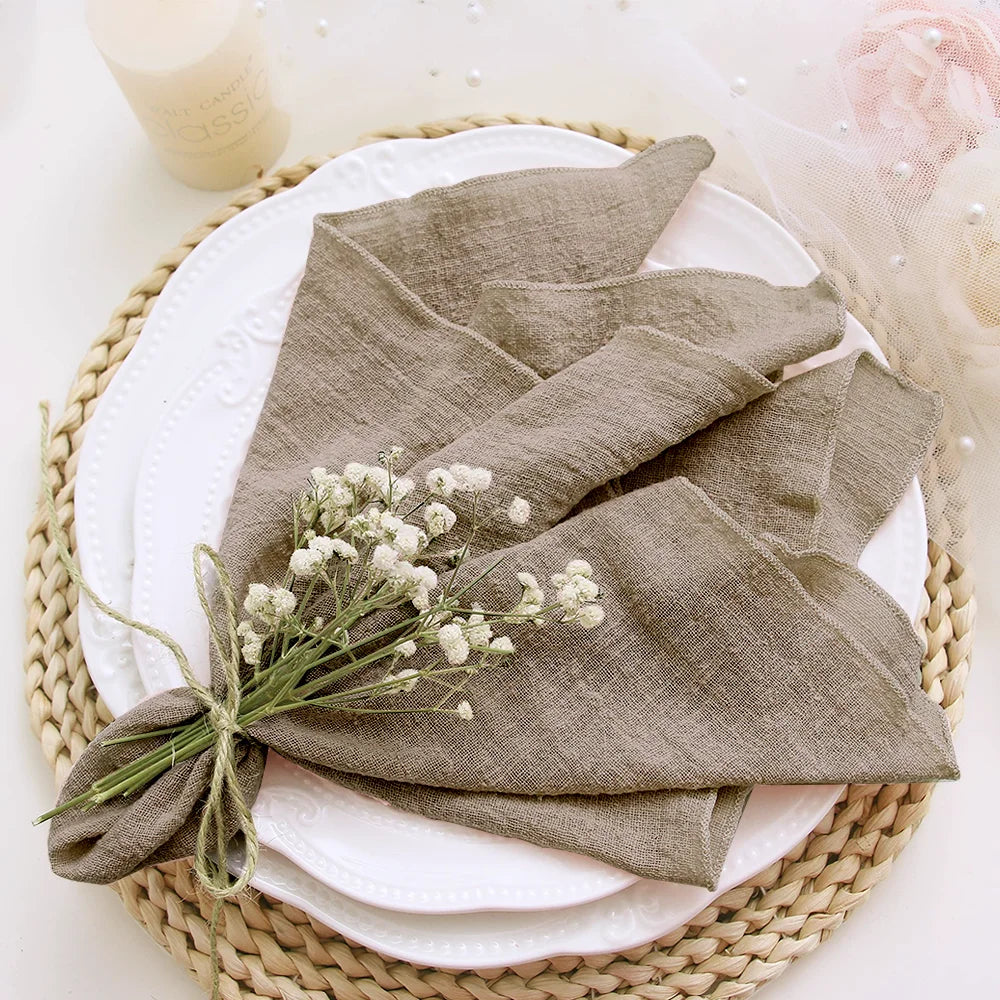 Folded brown napkin with a small bouquet of white flowers on a white plate with a woven placemat.