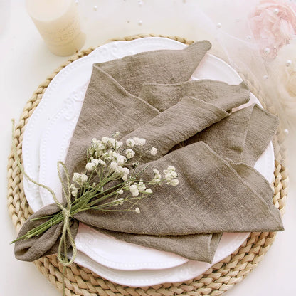 Folded brown napkin with a small bouquet of white flowers on a white plate with a woven placemat.
