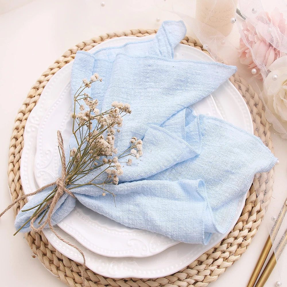 Light blue folded fabric on a white plate with dried flowers, on a woven placemat.