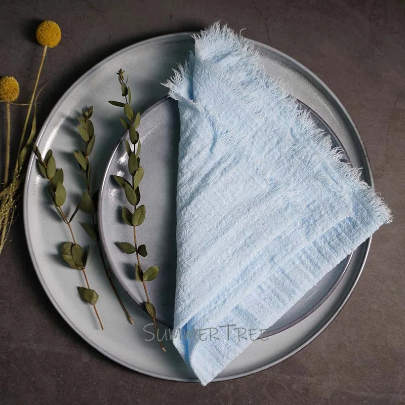 Light blue towel on a white plate with greenery and flowers on a dark surface