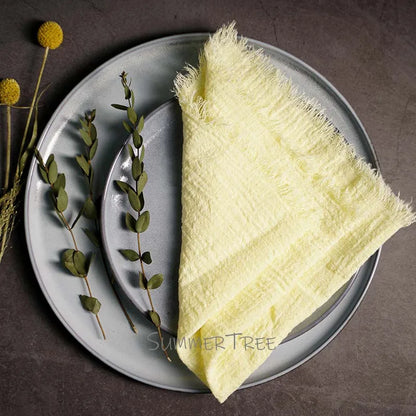 Light yellow textured towel on a gray plate with greenery, on a dark surface.
