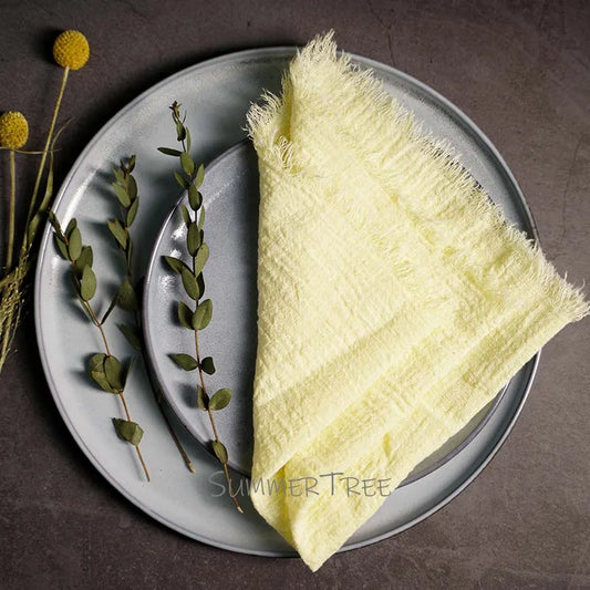 Light yellow textured towel on a gray plate with greenery, on a dark surface.