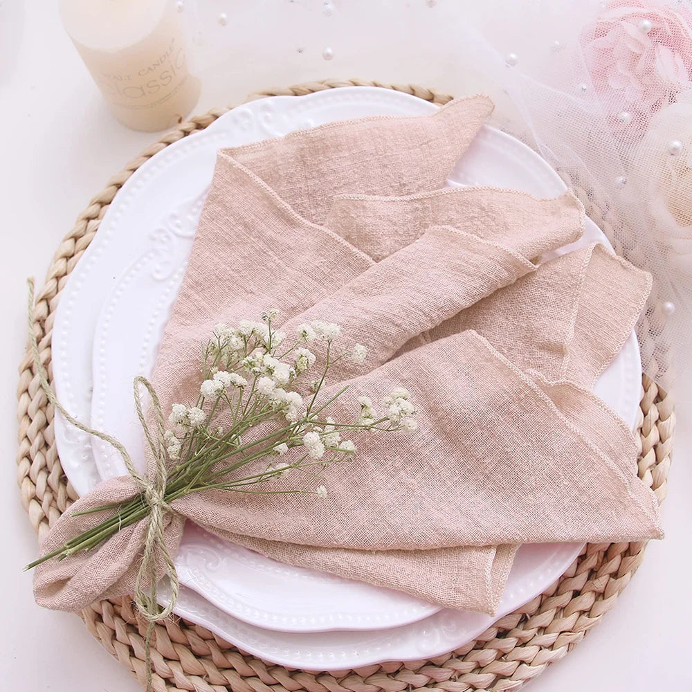 Folded beige napkin with a small bouquet of white flowers on a white plate, placed on a woven mat.