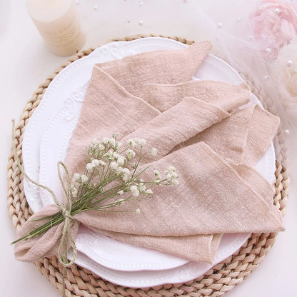 Folded beige napkin with a small bouquet of white flowers on a white plate, placed on a woven mat.