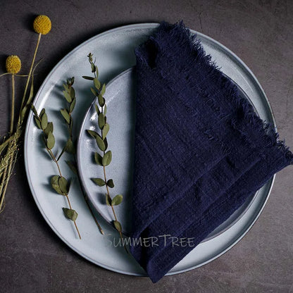 Navy blue napkin on a light blue plate with greenery and yellow flowers on a dark surface.