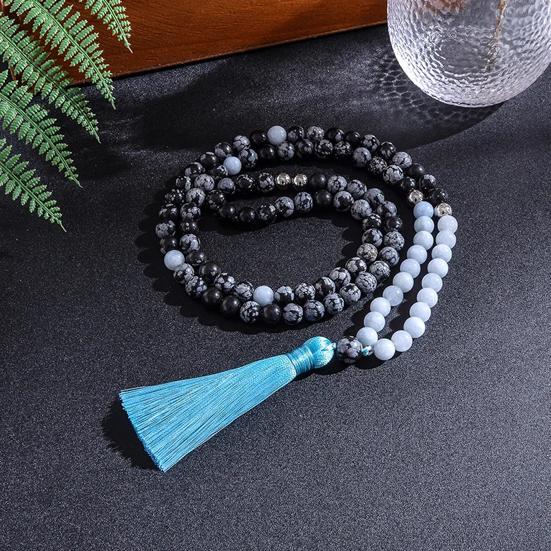 Mala necklace with blue tassel on a dark surface with greenery and a vase in the background