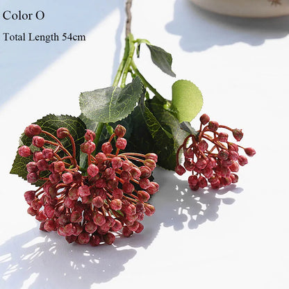 Artificial flower branch with pink berries and green leaves on a white surface.