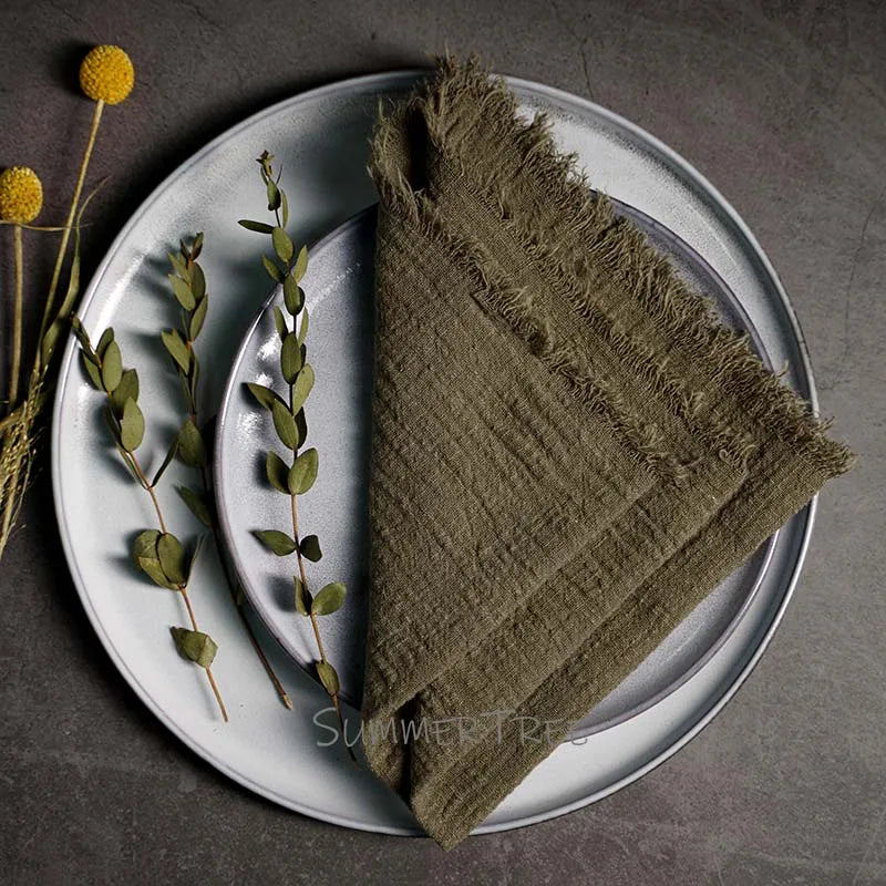 Brown napkin on a white plate with greenery and flowers on a dark surface