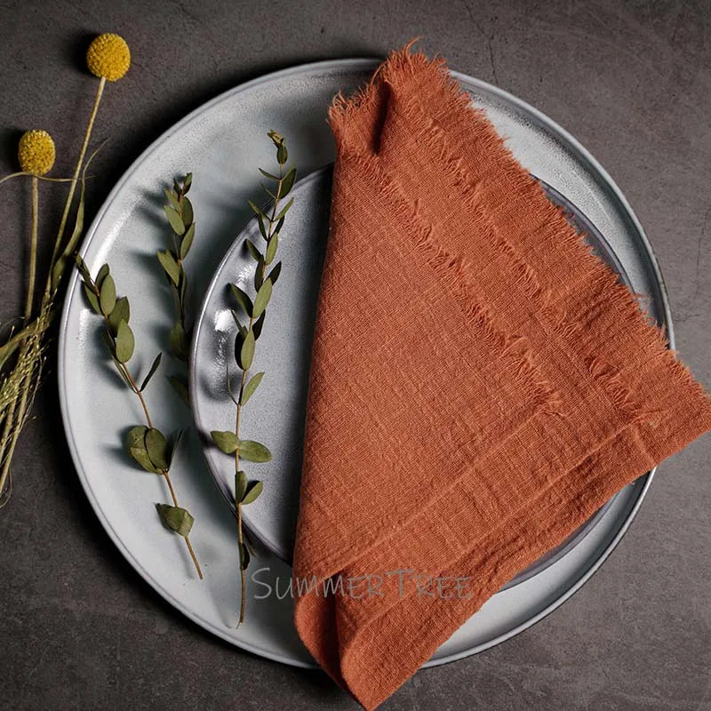 Rust-colored napkin on a gray plate with silverware and greenery, on a dark surface.
