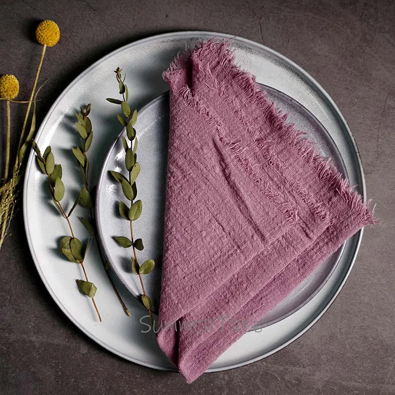 Pink textured napkin on a white plate with greenery and flowers on a dark surface