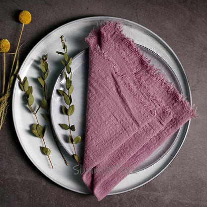 Pink textured napkin on a white plate with greenery and flowers on a dark surface