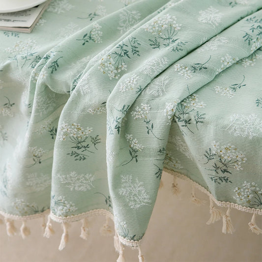 Green floral patterned tablecloth with tassels on a surface