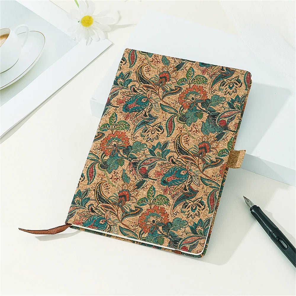 Floral patterned notebook on a white surface with a pen and cup in the background