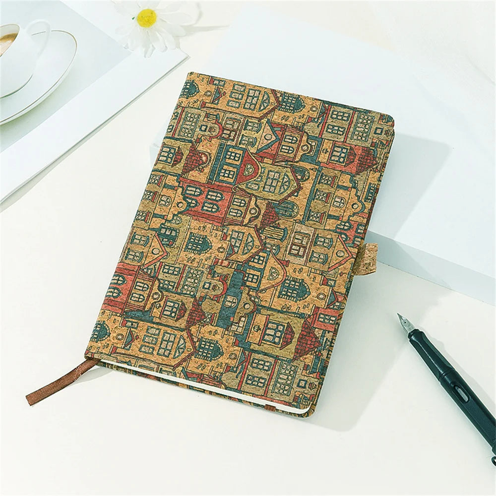 Notebook with decorative cover featuring house pattern on a white surface with a pen and cup.
