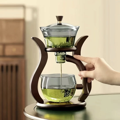 Glass teapot with wooden handle being used to pour green tea into another glass container.