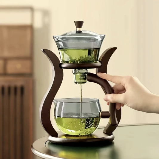 Glass teapot with wooden handle being used to pour green tea into another glass container.