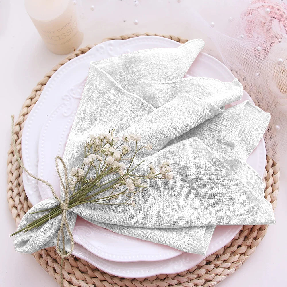 Folded light gray napkin with a small bouquet of flowers on a white plate, placed on a woven mat.
