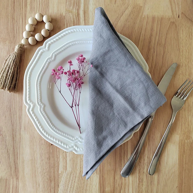 Dinner setting with a white plate, gray napkin, pink flowers, and cutlery on a wooden table.