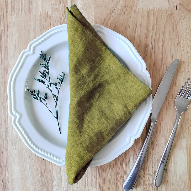 Green napkin on a white plate with cutlery on a wooden table