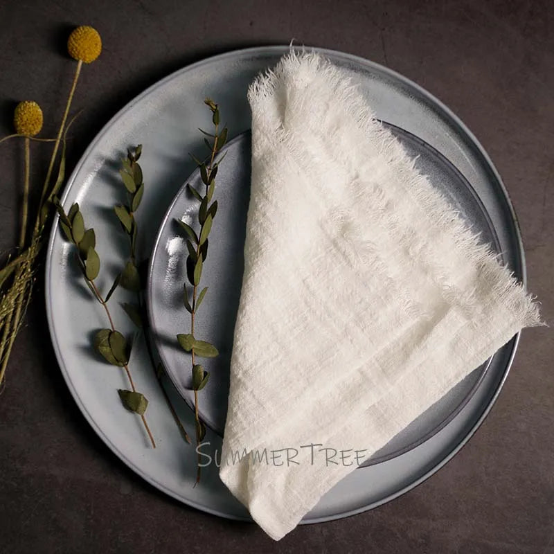 White textured napkin on a gray plate with greenery, on a dark surface.