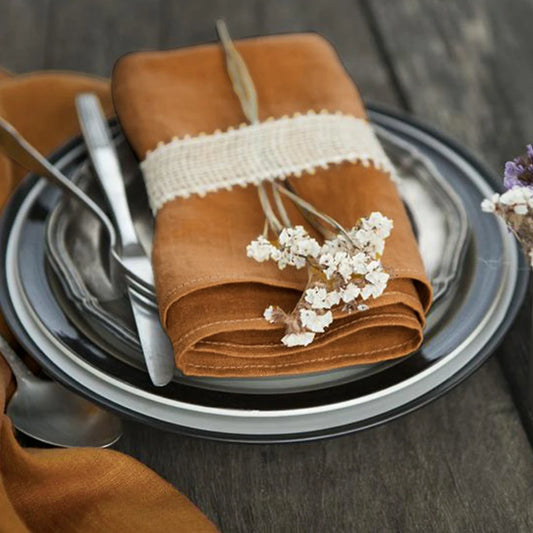 Brown napkin with white flowers on a stack of plates with silverware